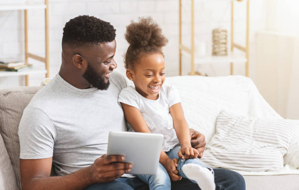 istock Smiling little girl using digital tablet with her dad 1202700994