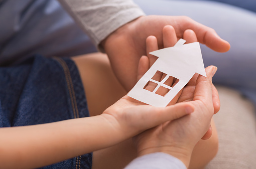 Real Estate And Family Housing Concept. Cutout paper house in hands of little girl and her parents, closeup