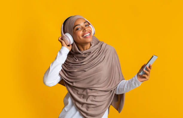 afro muslim girl listening music on smartphone with wireless headphones - traditional clothing audio - fotografias e filmes do acervo