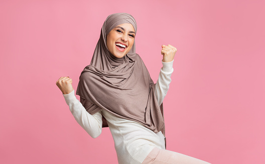 Yes. Happy muslim woman in hijab rejoicing success, raising hands and exclaiming with winner face expression