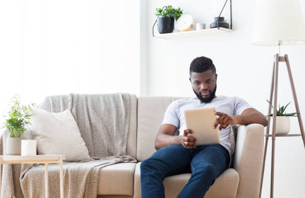 istock Young african man browsing on digital tablet at home 1202704999