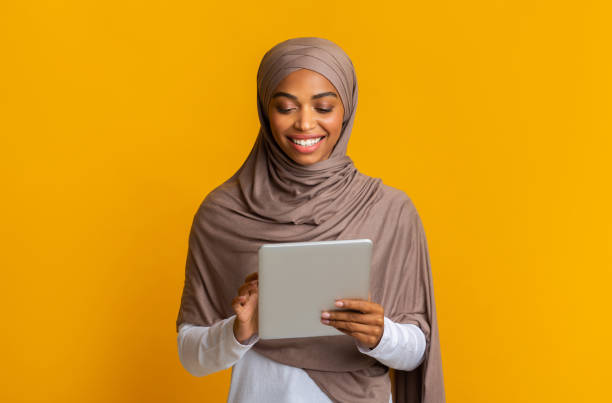 istock Smiling Black Muslim Girl Using Digital Tablet Standing Over Yellow Background 1202705105