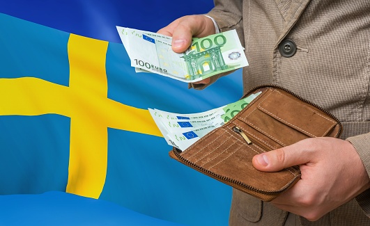 Investing money to Sweden. Rich man with a lot of money in his hands and national flag on background.