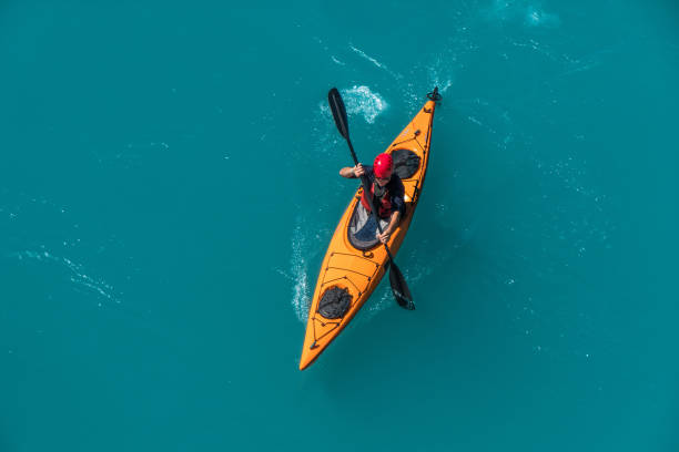 Seen from above|: a man paddles in an orange canoe on blue water. Photo was taken on the Raikaka river, Canterbury, South Island, New Zealand