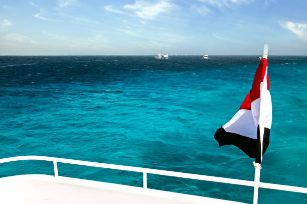 Egypt national flag waving on the wind of blue sky background. White yachts tourists in azure water Red sea, Arab Republic of Egypt.