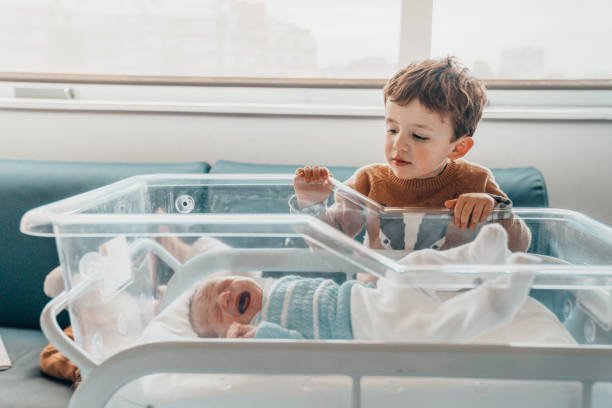 братья с�мотрят на нового младшего брата в больничной кроватке - new childbirth new life love стоковые фото и изображения