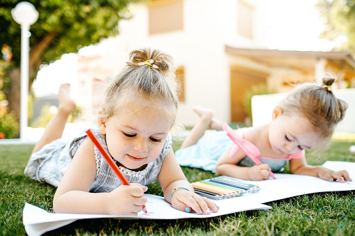 Little girls painting on drawing paper outdoors on grass