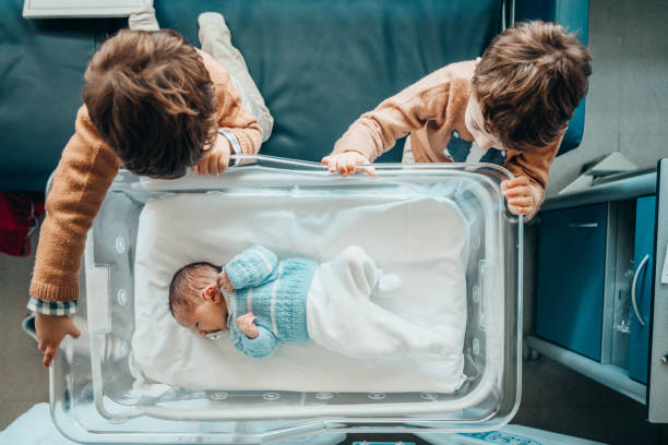 братья смотрят на нового младшего брата в больничной кроватке - new childbirth new life love стоковые фото и изображения