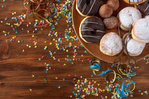 Sweet pastries for carnival and birthday. Flat lay photography on wooden surface with colorful confetti and streamers. Top view for a background konzept.