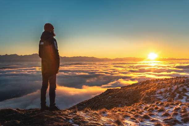 istock A man stands high in the mountains, at sunset, above the clouds. 1202716525