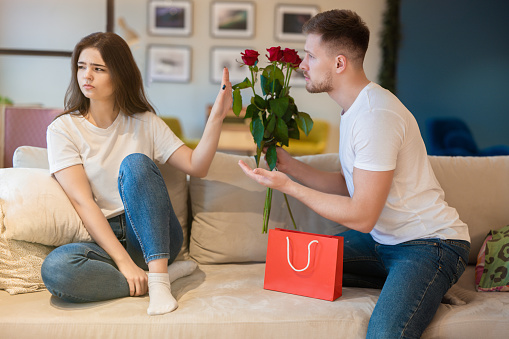 handsome man surprising his beautiful wife with roses after being guilty, she shows his back off sign.