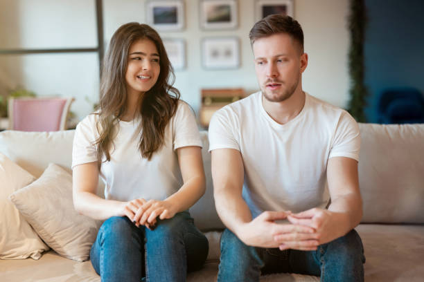 young couple man and woman sitting on the sofa both looking embarrassed , grimacing mood young couple man and woman sitting on the sofa both looking embarrassed , grimacing mood. uncomfortable stock pictures, royalty-free photos & images