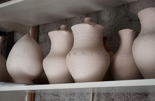 Handmade ceramic ceramics with glaze and without glaze. Pitchers and pots dry on shelves in a pottery workshop before the firing process.