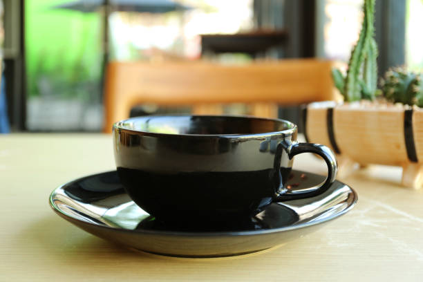 istock Black cup on wooden table with blurry coffee shop in background 1202721680