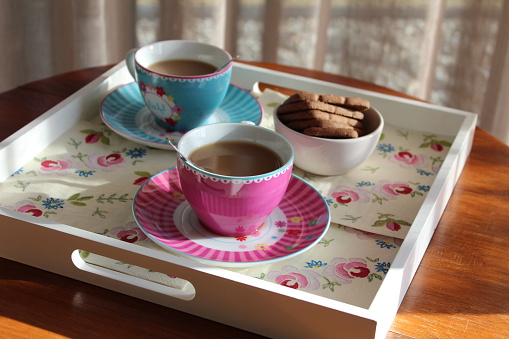 Closeup of two colored cups of coffee and some cookies on a white tray indoors