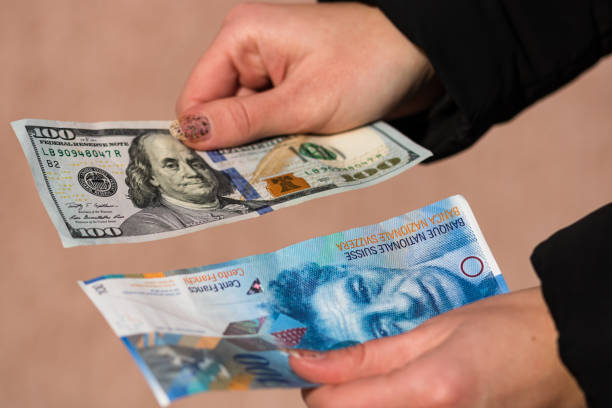 istock Hand holding money isolated on banknotes background. USD and CHF currency banknotes compared close up. Inflation, finance and business concept 1202724757