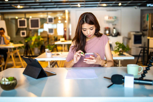 istock Taiwanese woman using mobile phone at modern open space workplace 1202725249