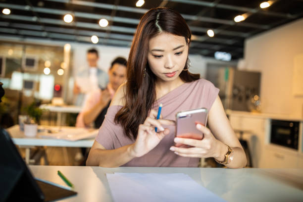 istock Taiwanese woman using mobile phone at modern open space workplace 1202725287