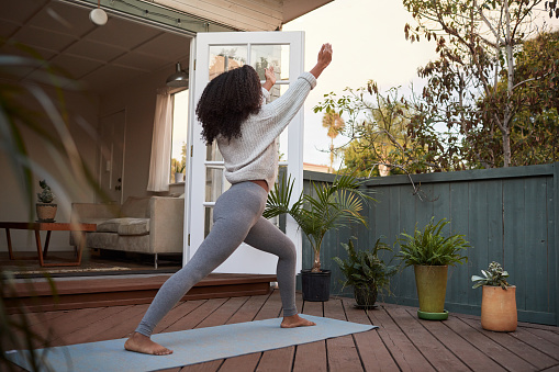 Young African American woman doing the crescent lunge pose during a yoga session outside on an exercise mat on her patio