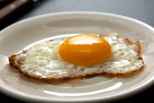 istock Fried egg close up in white plate. Breakfast food. Sunny side soft fried egg. 1202729852