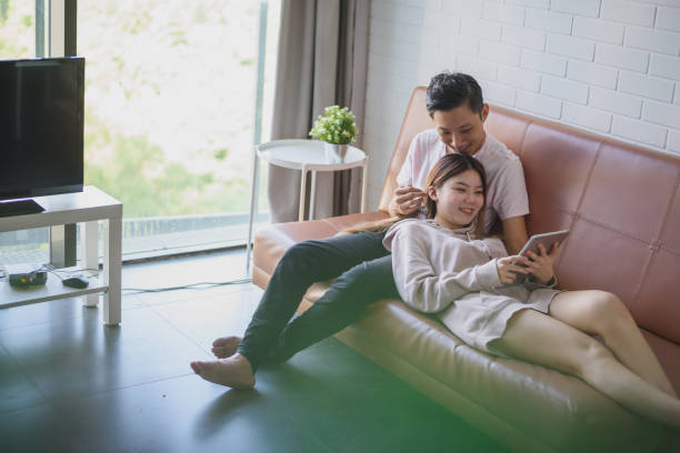 istock Happy Young Asian couple using digital tablet together on a sofa 1202730234