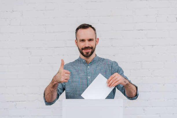 istock cheerful voter showing thumb up while holding blank ballot 1202730374