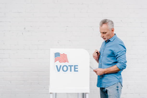 istock citizen holding pen while looking at ballot near voting stand 1202730384