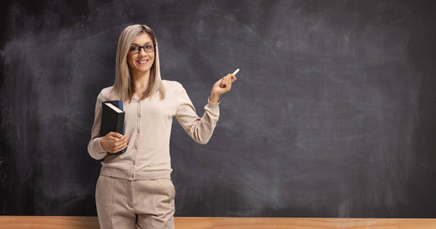 jeune professeur féminin devant un tableau noir et retenant une craie - professor teacher female blackboard photos et images de collection