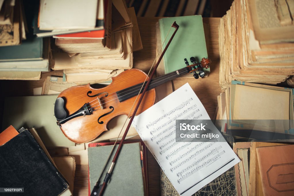 Vintage library still life with violin Library with archive of very old books and documents stored and unsorted and one violin. Mess that looks beautiful. Music Stock Photo