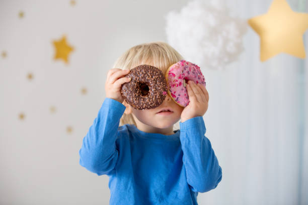 istock Cute sweet blonde child, playing and eating donuts 1202734532