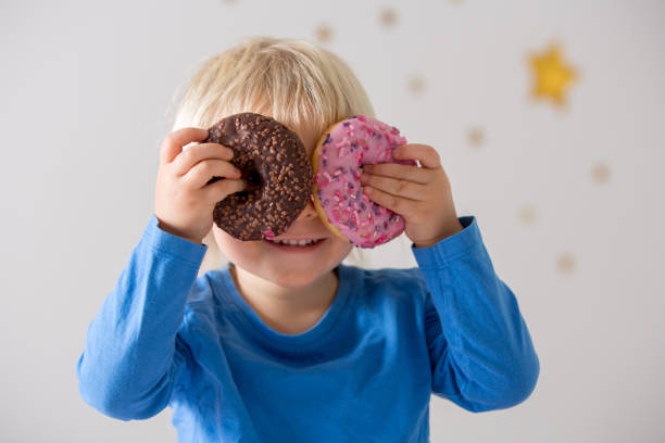 istock Cute sweet blonde child, playing and eating donuts 1202734675