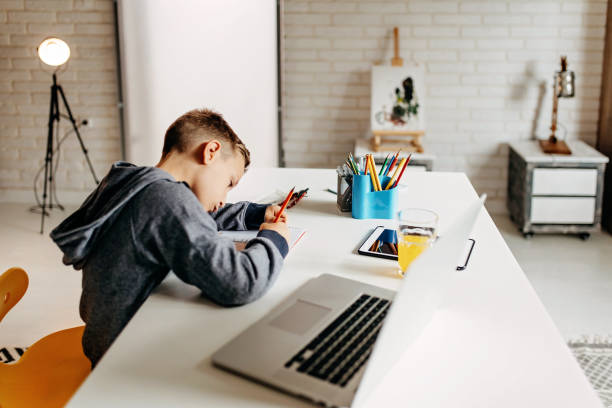 istock Young boy at home writing in school text book at the dining table 1202736486