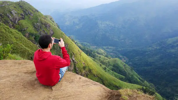 Photo of a guy photographs a mountain landscape sitting on the edge.