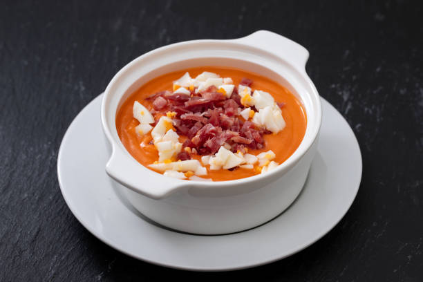 Typical Spanish soup salmorejo cream with ham and egg in white bowl on ceramic background. Top view.