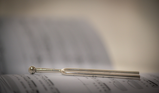 Tuning fork lies on old, historical notes. Bright background. Selective sharpness