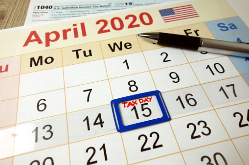 Tax day marked on April 2020 monthly calendar with 1040 form and pen