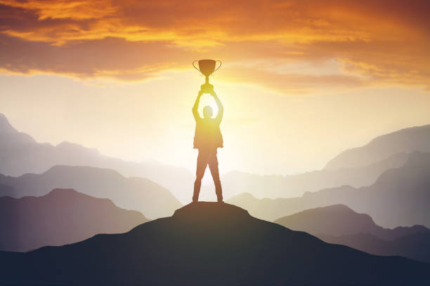 silhouette eines mannes, der eine trophäe bei sonnenuntergang hält - award trophy success achievement stock-fotos und bilder