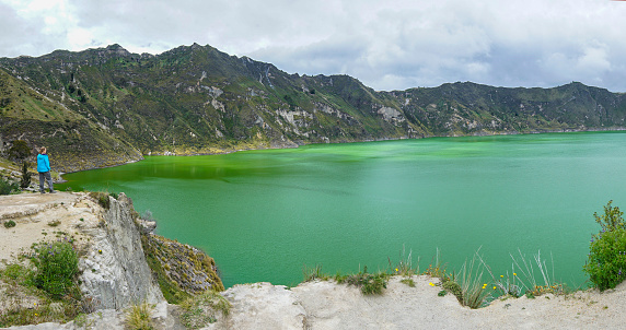 Panoramic View, Senior woman enjoying at caldera of the Quilotoa volcano lake. It is  3ooo m wide, about 250 deep and on the Elevation 3,914 m. The greenish color coms from dissolved minerals and it is touristic destination with hiking down to the lake.
