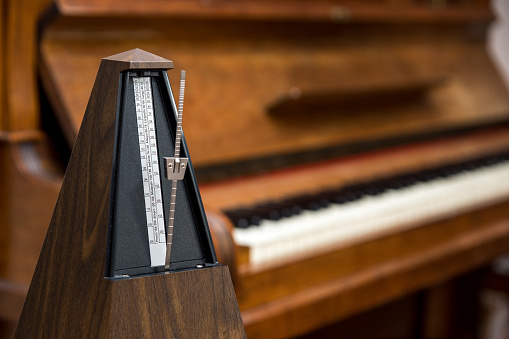 old, analog metronome, in front of an old piano in the background. Selective sharpness