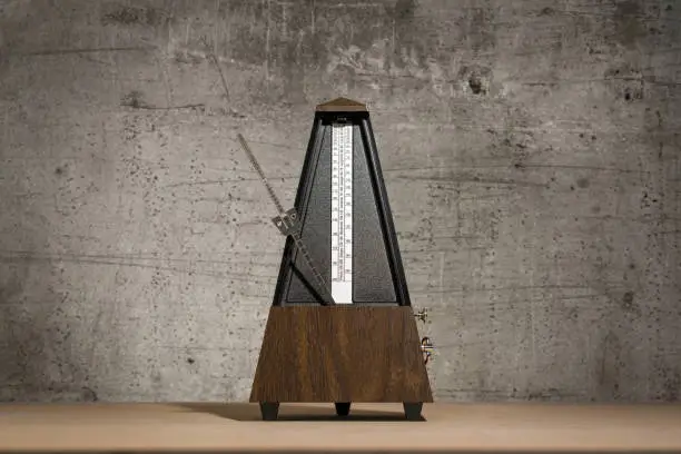 old, analog metronome, isolated against a concrete background with space for text