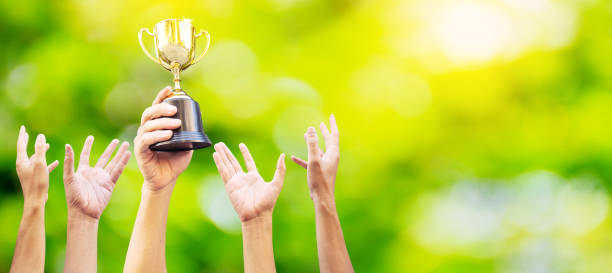 istock Many hands raised up. Winner is holding trophy cup in hand. on blurred green background