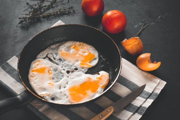 istock fried eggs in a pan on a towel, thyme, tomatoes, shell, knife on a black background 1202747191