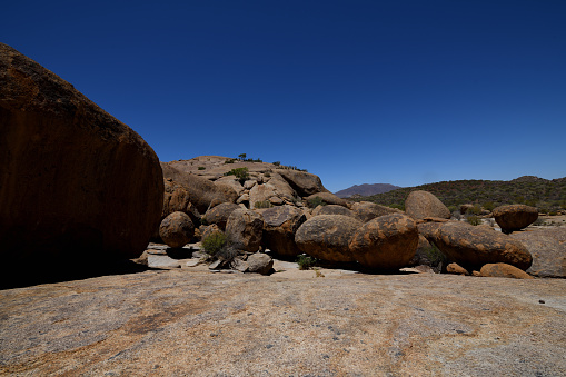 The boulders are the result of millions of years of weathering of granite rock, and are called a ‘woolsack formations’. In the foreground is a woolsack boulder.The sky is blue.\n\nThe area of Bulls Party is reached through the Amieb Guest Farm, near Erongo Mountains in Namibia. It is littered with the results of millions of years of weathering and is geologically interesting because of this. The photo was taken in March 2019.