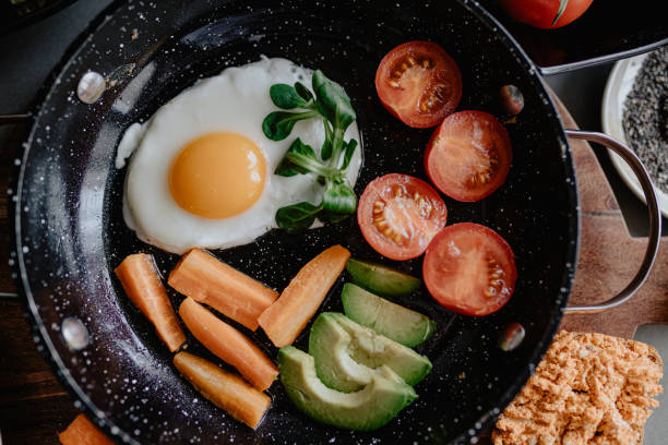 Preparing for breakfast fried egg with carrots, avocado, cherry tomato and corn salad in frying pan