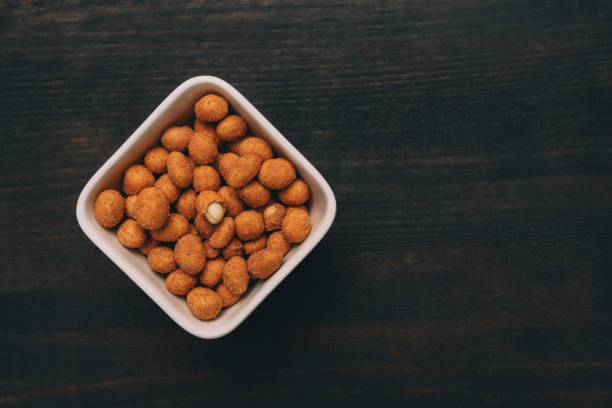 Salty peanut snack coated with barbecue sauce served in ceramic bowl on table, top view