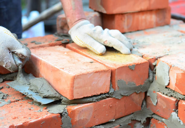 istock Bricklayer hands in masonry gloves with trowel laying bricks house wall. 1202755601