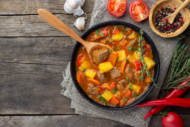 Goulash, beef stew or bogrash soup with meat, vegetables and spices in cast iron pan. Goulash, beef stew or bogrash soup with meat, vegetables and spices in cast iron pan on wooden table. Hungarian cuisine. Rustic style. Top view. hungary stock pictures, royalty-free photos & images