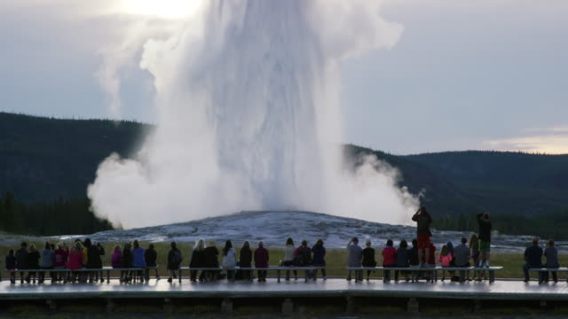 Slow Motion Shot of a Crowd of People Watching Old Faithful Geyser Erupt in Yellowstone National Park on an Overcast Day