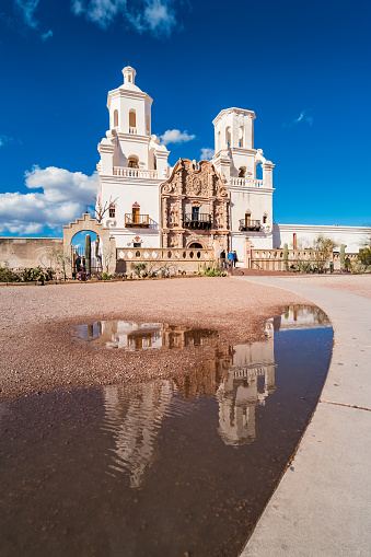 Mission San Xavier del Bac Church in Tucson Arizona reflecting in a rain puddle on a sunny day .