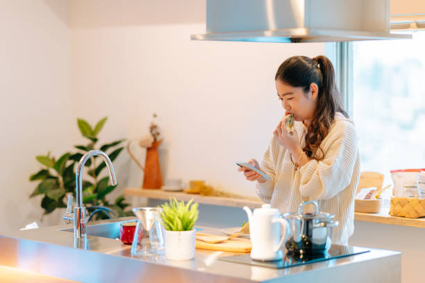 istock Young woman checking smart phone while eating breakfast 1202760212